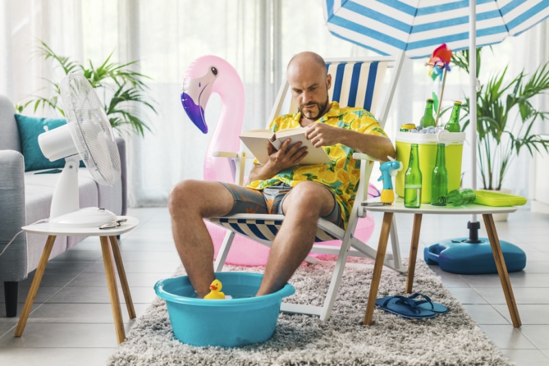 man with beach setup in his living room reading a book
