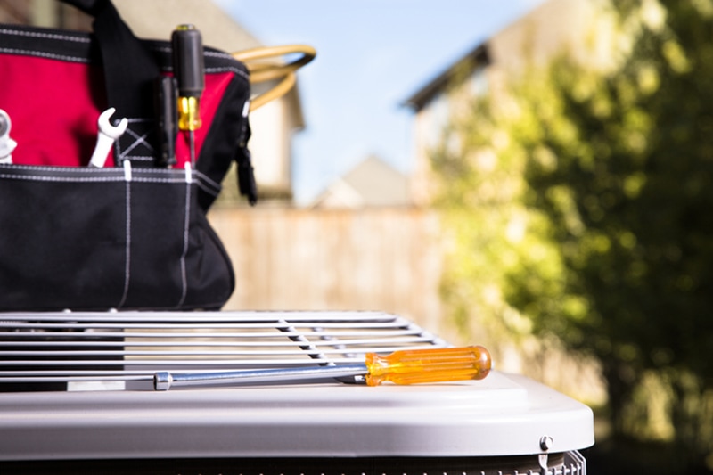Blog Title: Common AC Problems and Solutions Photo: Bag of repairman's work tools, screwdriver on top of air conditioner unit.