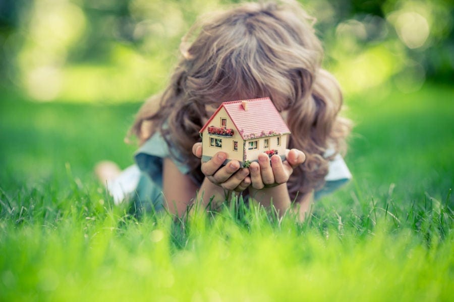 Young girl laying in the grass holding little home.